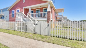 A two-story house with a red exterior, white porch railing, and a white picket fence.