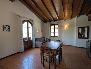 Une pièce avec un plafond en bois, une table à manger avec des chaises, un canapé, une grande fenêtre en arc de cercle et un miroir fixé au mur.
