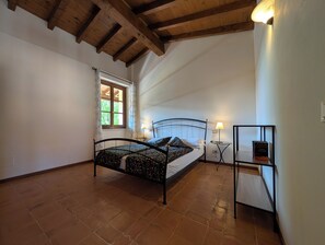 A bedroom with a bed, a window, a nightstand, a lamp, and a shelf with a book.