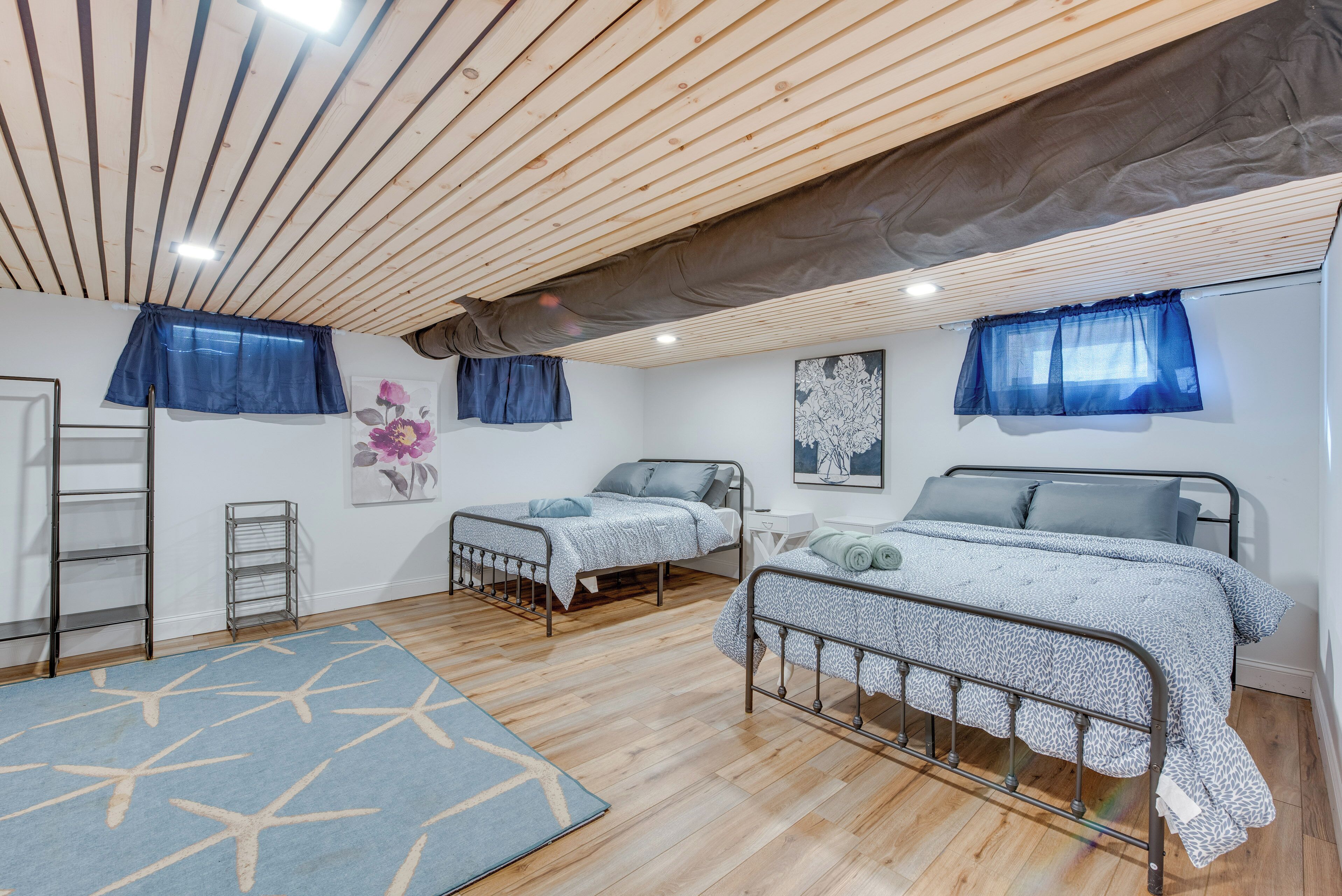 A bedroom with two beds, a wooden ceiling, and a blue patterned rug.