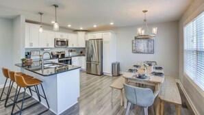 A modern kitchen with white cabinets, stainless steel appliances, and a dining area with a wooden table and bar stools. - Lovely Scottsville Home, Minutes to Bowling Green (Scottsville)