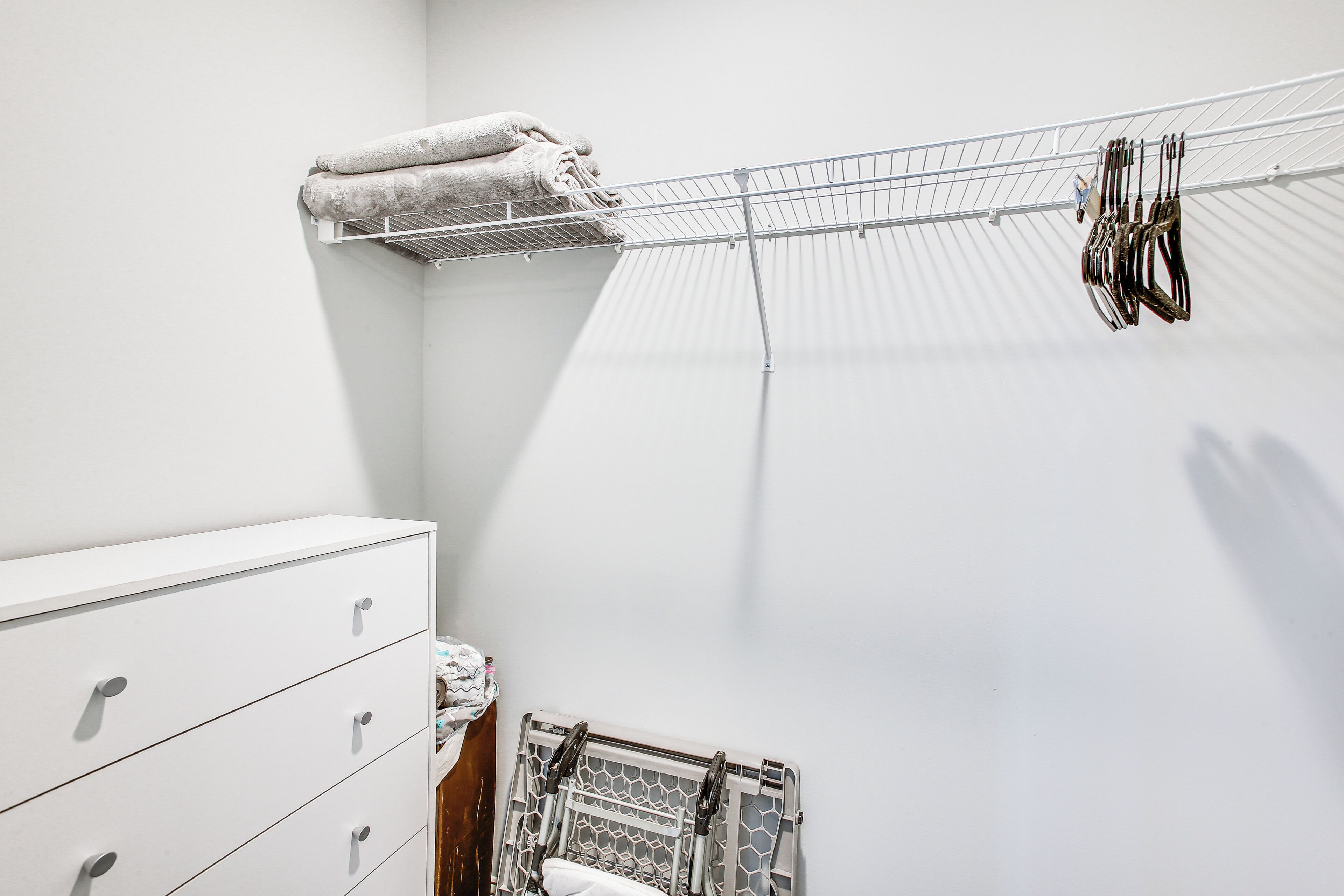 Un espace dédié à la lessive, comprenant un étendoir, une commode blanche et un séchoir métallique sur lequel sont suspendus des vêtements et des cintres.