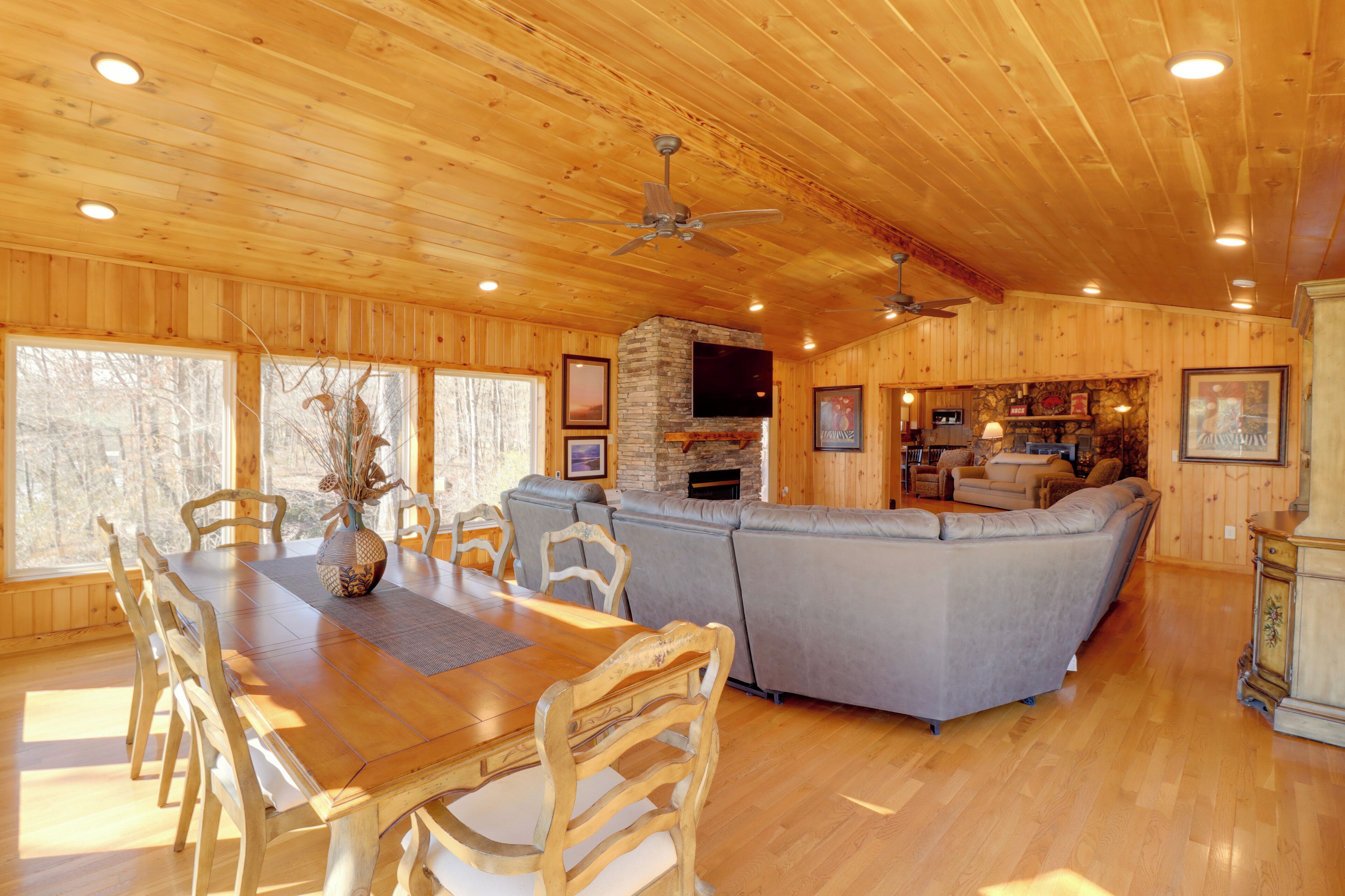 A wooden interior with a dining table, chairs, a grey sofa, and a fireplace.