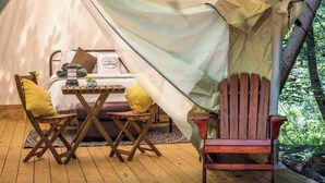 A cozy tent with a bed, a table, and two chairs.