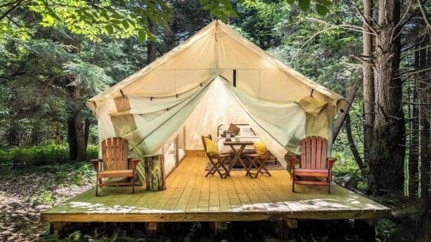A tent with a wooden deck, two chairs, and a table.