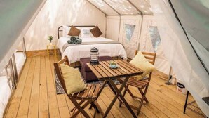 A tented accommodation with a bed, a small table, and two chairs.