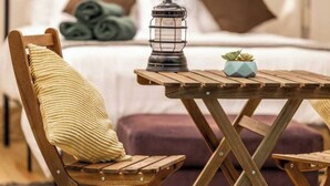 A wooden chair with a striped cushion, a small table with a lantern and a plant, and rolled towels in the background.