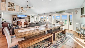 Un salon spacieux avec une grande table en bois, des sièges confortables et une vue sur la ville grâce à de grandes fenêtres.