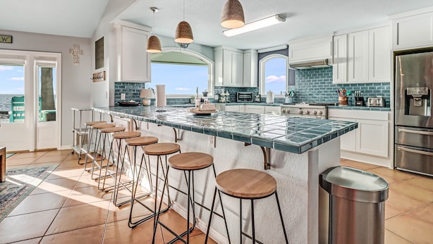 Une cuisine moderne dotée d’un grand îlot central, de tabourets de bar, d’appareils électroménagers en acier inoxydable et offrant une vue sur l’extérieur.