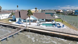 Une propriété située au bord de l’eau, dotée d’une piscine, de chaises longues et d’un petit bâtiment dont le toit est recouvert de chaume.