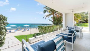 A balcony with a view of the beach, outdoor seating, and a dining area. - Rum Point Resort 106 by Grand Cayman Villas (Grand Cayman)