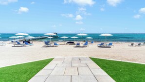 A beach with lounge chairs and umbrellas, a clear sky, and the ocean in the background. - Rum Point Resort 106 by Grand Cayman Villas (Grand Cayman)