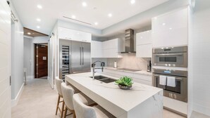 A modern kitchen with white cabinetry, stainless steel appliances, and a marble countertop island with bar stools. - Rum Point Resort 106 by Grand Cayman Villas (Grand Cayman)