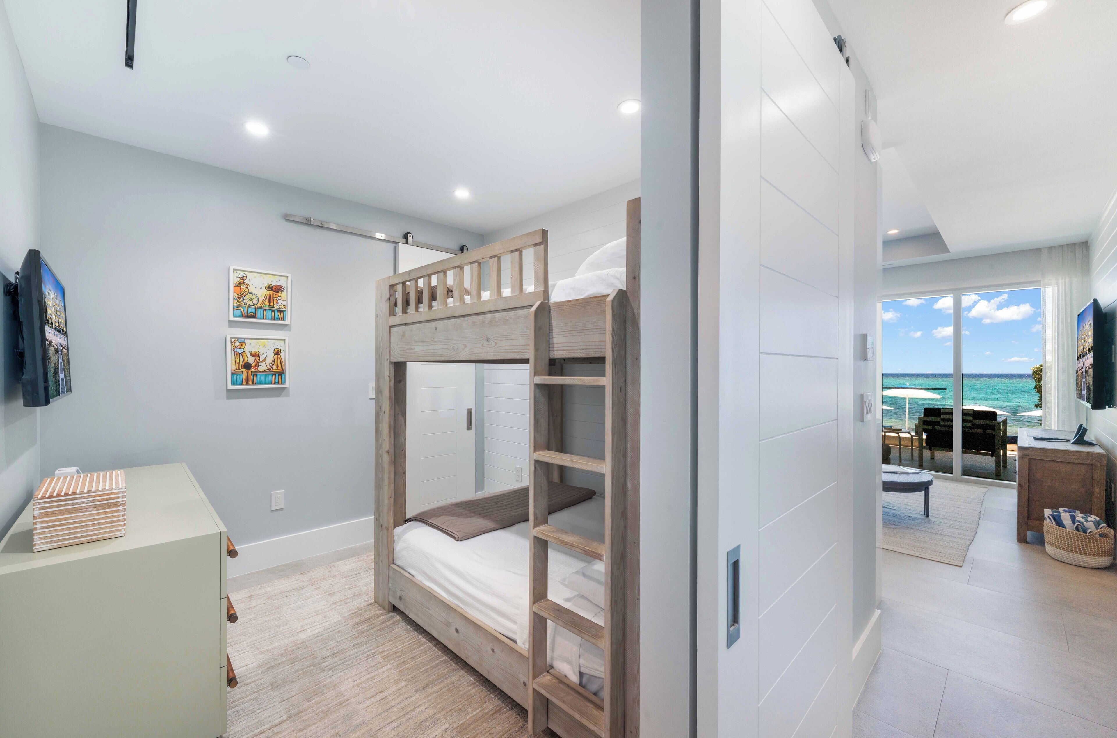 A modern bedroom with a bunk bed, a desk, and a view of the ocean.