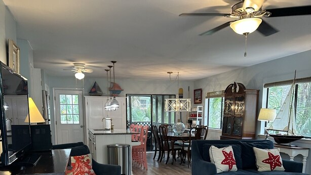 Un vaste salon doté d’un plancher en bois, de deux canapés ornés de coussins à motifs étoilés, d’un coin repas avec une table à plateau en verre et d’un ventilateur de plafond.