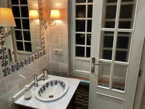 Een badkamer met een wit wastafel, een spiegel en een matglazen deur.