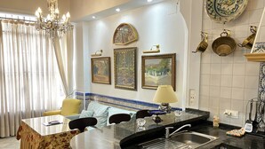 A modern kitchen with a marble countertop, a built-in sink, and a dining area with a table and chairs. There are decorative plates and a chandelier visible. - Estudio en Casa Palacial (Sevilla)