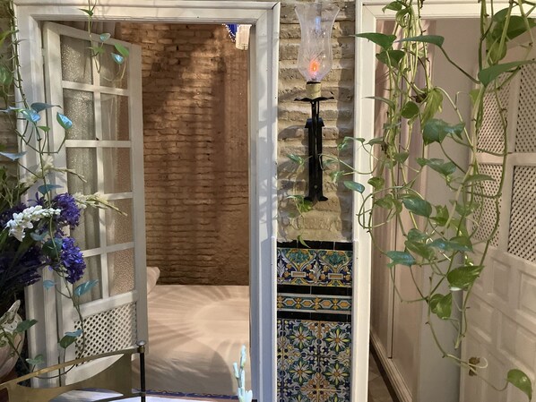 A room with a brick wall, a decorative light fixture, and hanging plants. - Estudio en Casa Palacial (Sevilla)