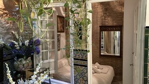 A room with a bed, a window with a view, and a hanging plant. - Estudio en Casa Palacial (Sevilla)