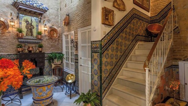 A traditional interior with a staircase, tiled walls, and decorative items. - Estudio en Casa Palacial (Sevilla)