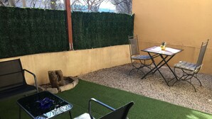 Een terras buiten met kunstgras, een tafel, twee stoelen en een houten constructie.