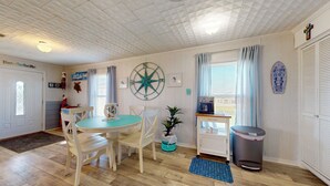 Ein Zimmer mit einem runden Tisch, weißen Stühlen, einer Kaffeemaschine, einem Mülleimer und einem fenster mit Vorhängen.