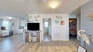 Ein Zimmer mit einem Fernseher auf einem Holzständer, einer kleinen Ablage mit Dekorationsobjekten, einer Tür zu einem anderen Raum und einer Wand mit verschiedenen gerahmten Bildern und Schildern.