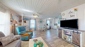 Ein geräumiges Wohnzimmer mit Fernseher, einem Essbereich und einer Küche im Hintergrund.