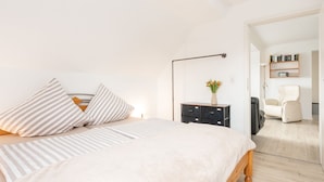 A bedroom with a bed, bedside table, lamp, and a chair in a hallway. - Vacation in the countryside - adventure and relaxation - what (Schellhorn)
