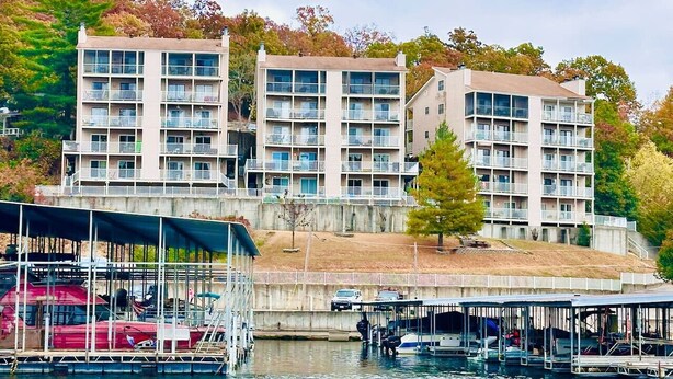 A waterfront property with multiple-story buildings, docked boats, and a covered boat launch area. - Wheelhouse: Lakefront 2BD/3BA/Deck/Pool/Pet Friendly-6PP (Lake Ozark)