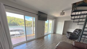 A spacious living room with a large sliding glass door leading to a balcony with a view of a lake. - Wheelhouse: Lakefront 2BD/3BA/Deck/Pool/Pet Friendly-6PP (Lake Ozark)