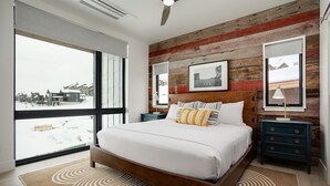 Un dormitorio moderno con una cama grande, cabecera de madera y vistas a un paisaje nevado a través de amplios ventanales.