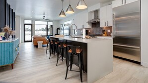 Una cocina moderna con una isla grande, taburetes de bar, electrodomésticos de acero inoxidable e iluminación colgante.
