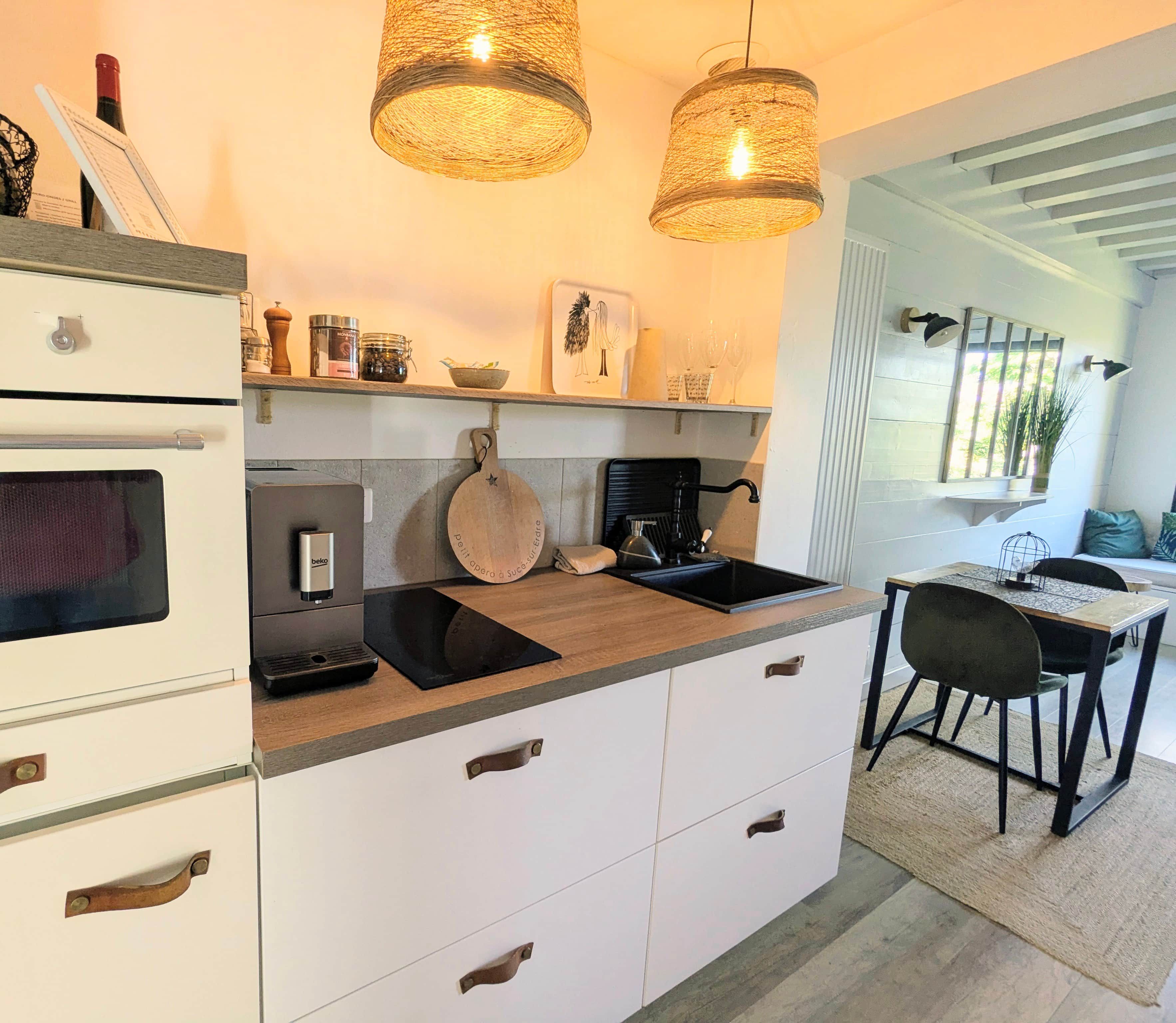 A modern kitchen with white cabinets, a black induction cooktop, a built-in oven, and a dining area with a table and chairs.
