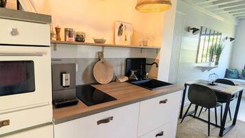 A modern kitchen with white cabinets, a black induction cooktop, a built-in oven, and a dining area with a table and chairs.
