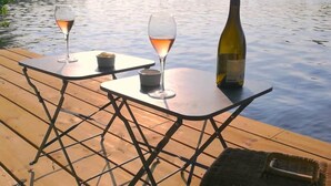 A wooden deck with two tables, each with a glass of wine and a bottle of wine.