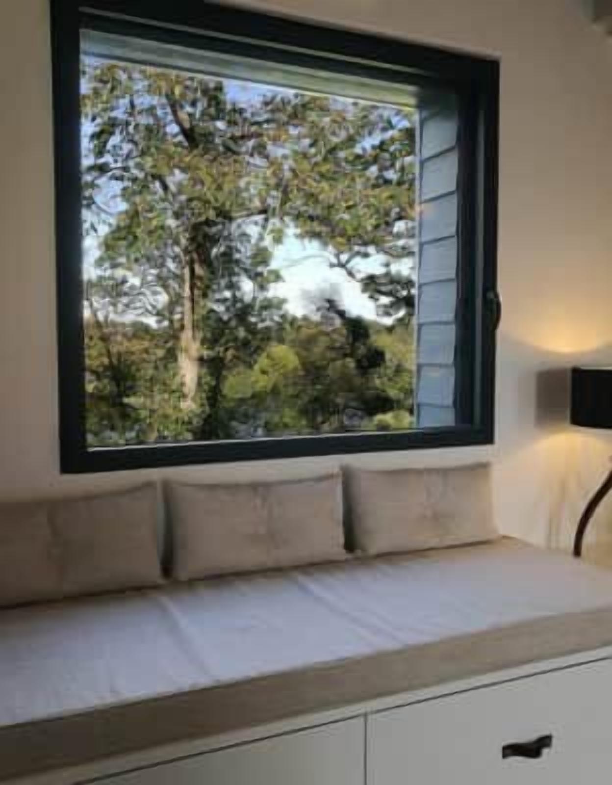 Um quarto com janela, cama com cabeceira e mesa de cabeceira.