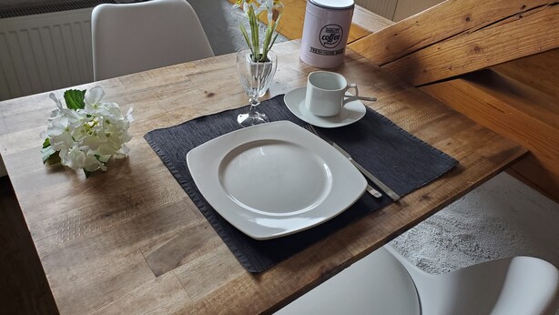 Ett träbord med en vit tallrik, ett glas, en kopp och en vas med blommor.