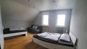 Ett sovrum med en säng på ett loft, en liten soffa och ett fönster.