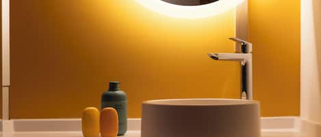 A bathroom with a white sink, a mirror with a circular light, and two bottles of soap on the counter.