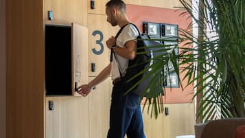 Una habitación de hotel moderna con un panel de pared de madera, puertas numeradas, un televisor y una planta grande.