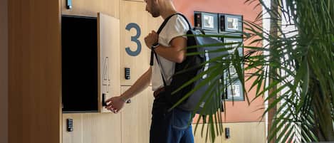 Una habitación de hotel moderna con un panel de pared de madera, puertas numeradas, un televisor y una planta grande.