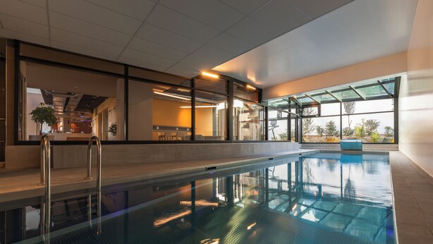 Una piscina interna con pareti in vetro trasparente, pavimento piastrellato e design moderno.