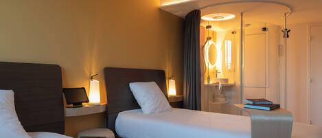 A hotel room with two beds, a bedside table with a lamp, a mirror, and a door with a circular mirror.