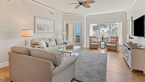 A spacious living room with a large sofa, a coffee table, and a ceiling fan. There are two chairs and a TV mounted on the wall. - Oceanfront 2 bedroom villa in Palmetto Dunes with Community Pool (Hilton Head Island)