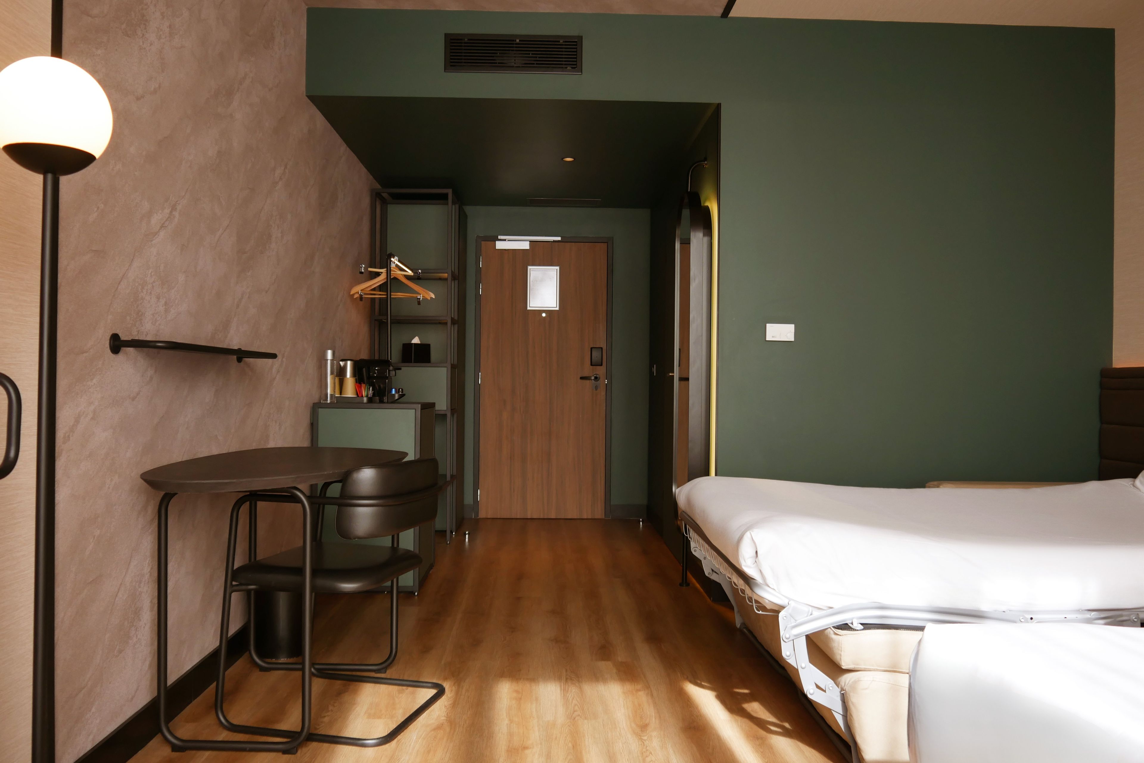 A hotel room with a bed, a desk, a chair, a wardrobe, and a hanging coat rack.