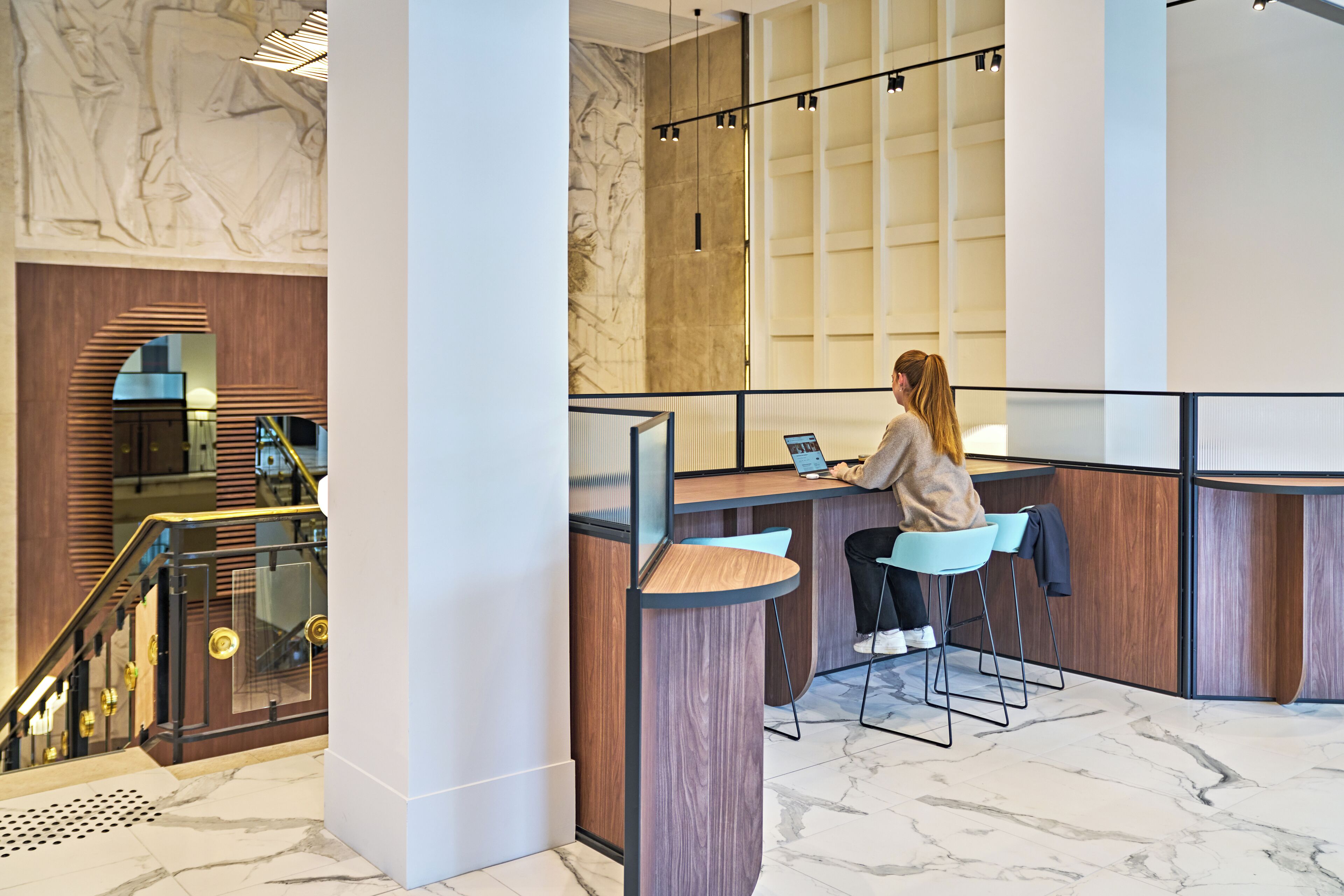 A modern reception area with a marble floor, wooden reception desk, and a staircase with a glass railing.