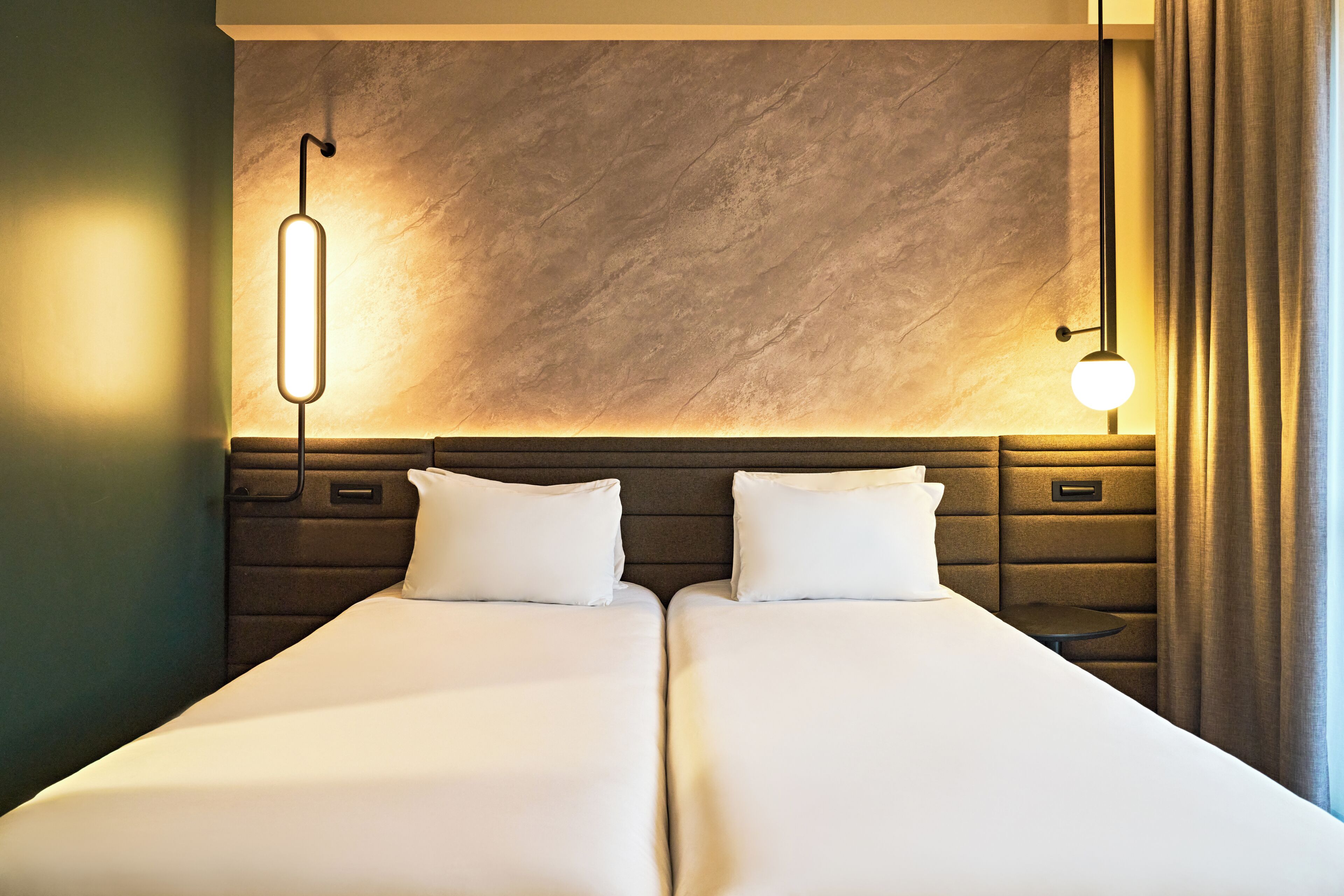 Un lit double avec une tête de lit, des tables de chevet et des lampes fixées au mur.