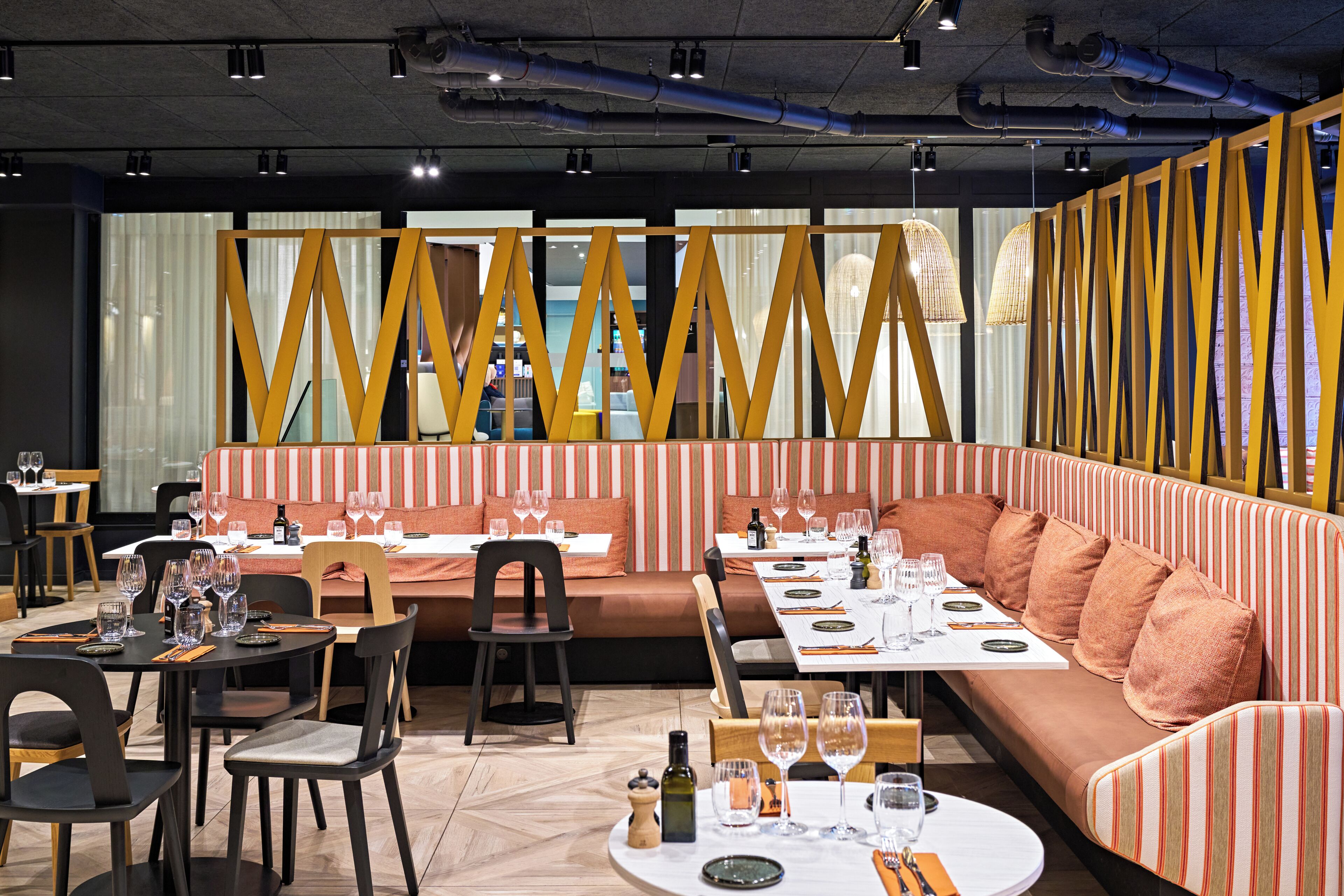 A restaurant with tables set for dining, a sofa area, and a view through a patterned partition.