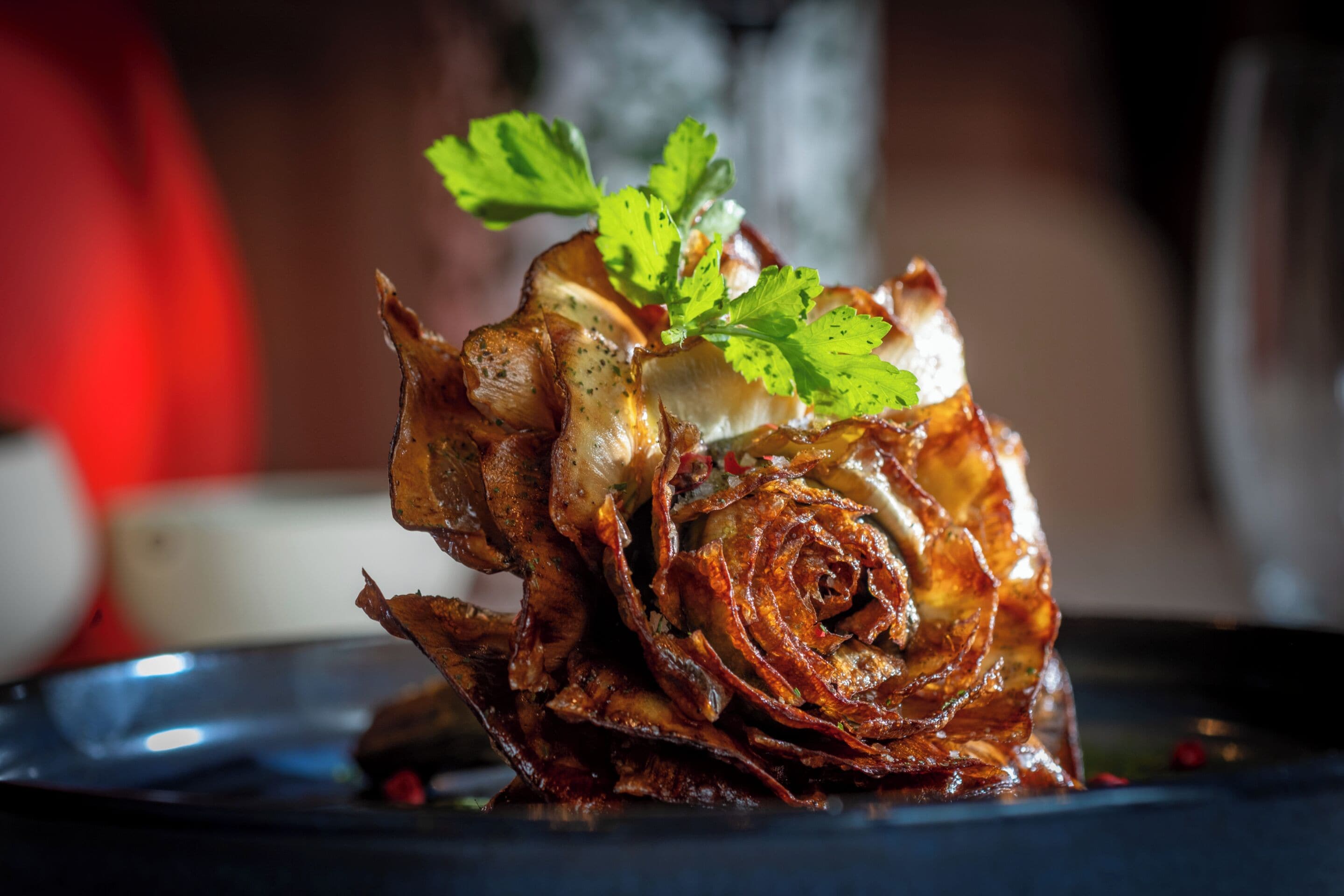 A dish with a spiral pattern, garnished with green leaves, served on a dark plate.